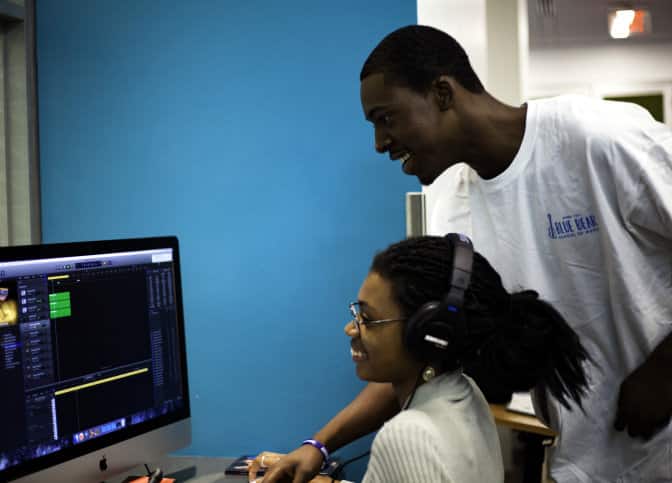 A student and instructor smile as they use music software.